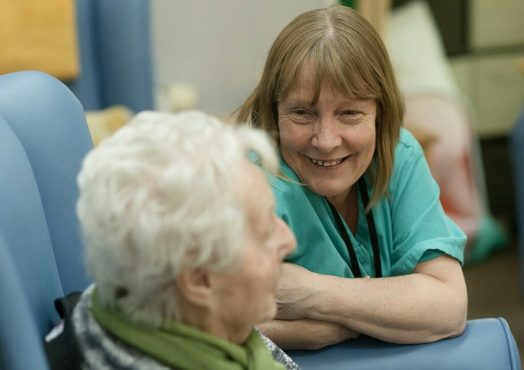 Smiling care worker leaning in to chat with an elderly woman in a chair
