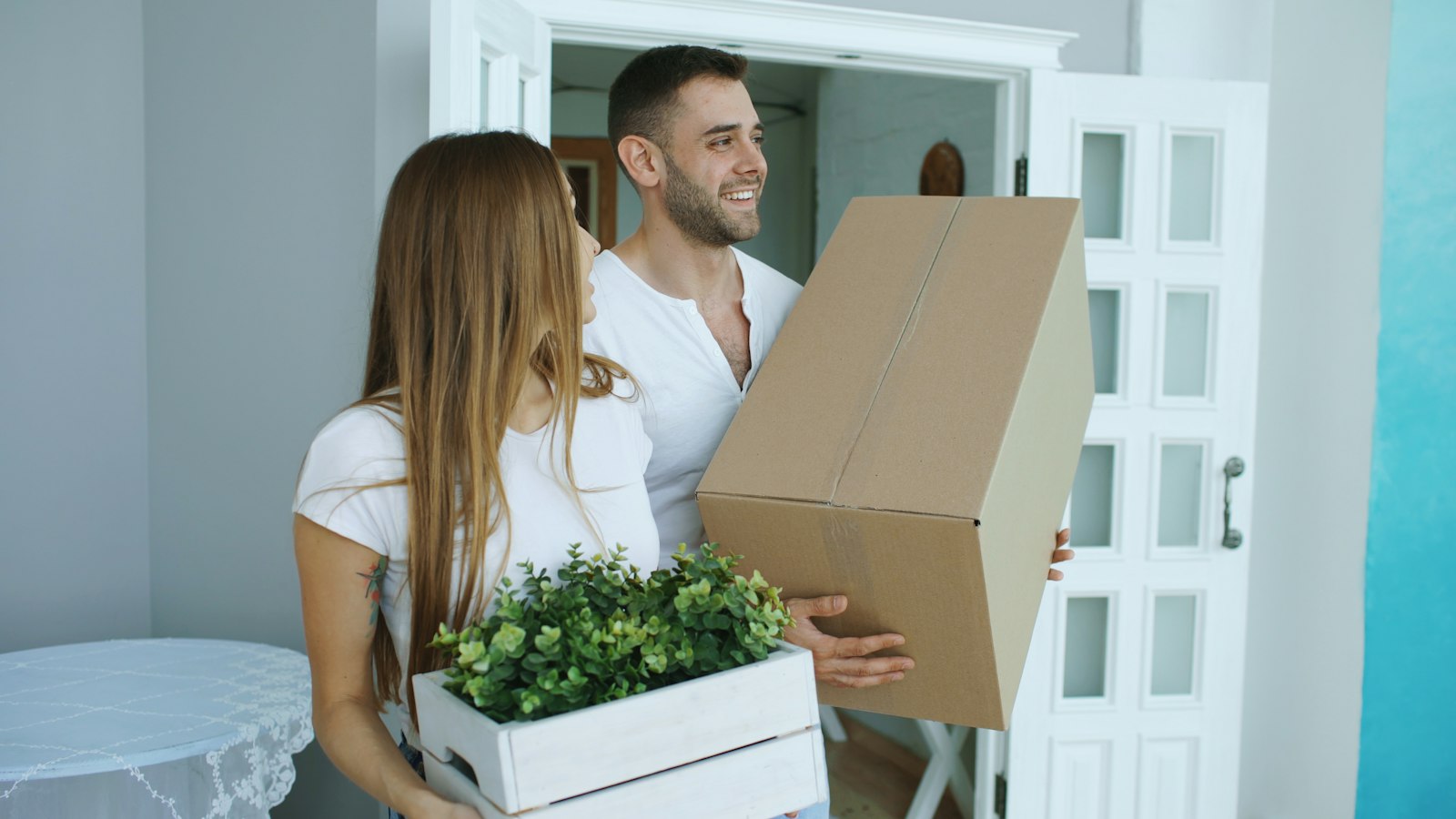 Couple carrying a cardboard box and a potted plant into their new home